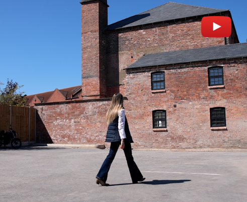 Woman walking in a paved lot beside a brick building with a blue sky overhead.